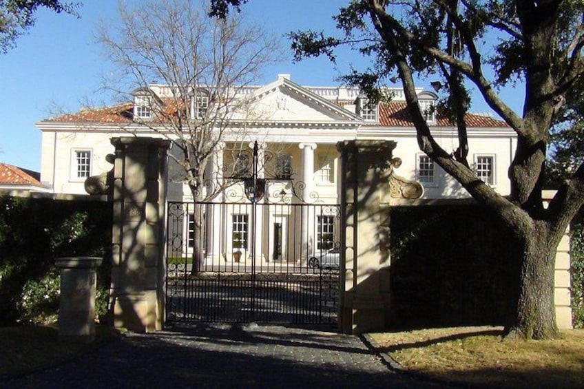 A stately white building with columns, a gated entrance, and a large tree in the foreground. 3
