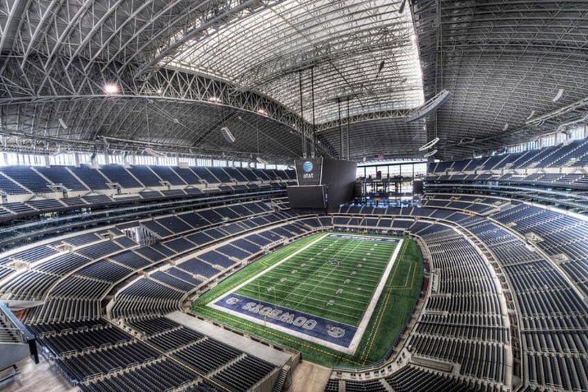 A large indoor stadium with multiple tiers of seating, a football field, and a large scoreboard. 1