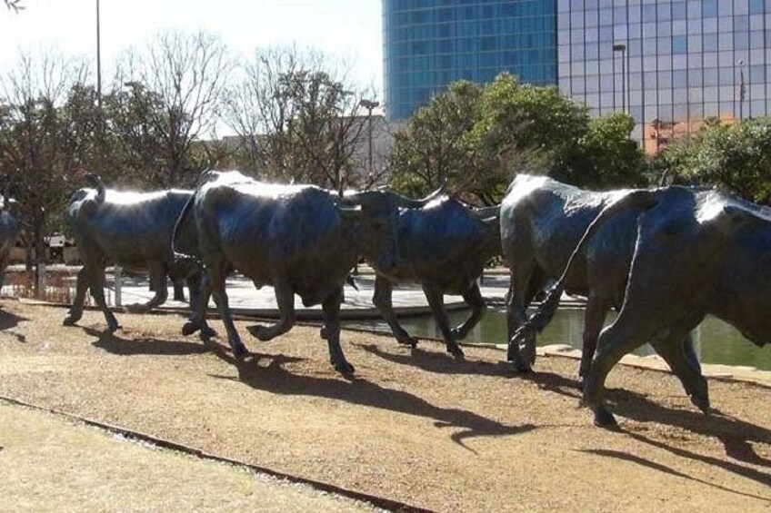 A row of metallic cow statues on a paved path. 3