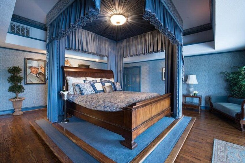 A four-poster canopy bed with a wooden headboard, blue drapery, and a nightstand with a lamp. 2