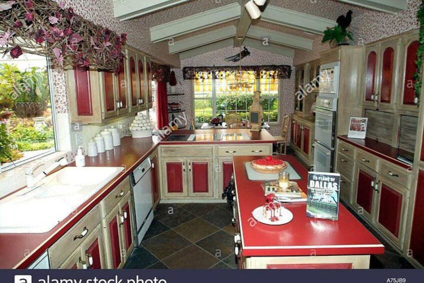 A vintage kitchen with red cabinets, a central island, and a window overlooking a garden. 3