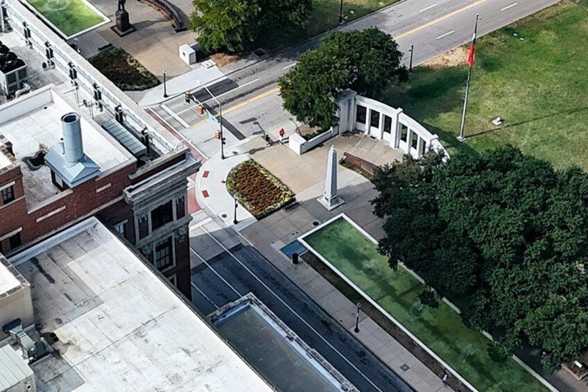An aerial view of a city intersection with buildings, a road, and a grassy area with a monument. 4