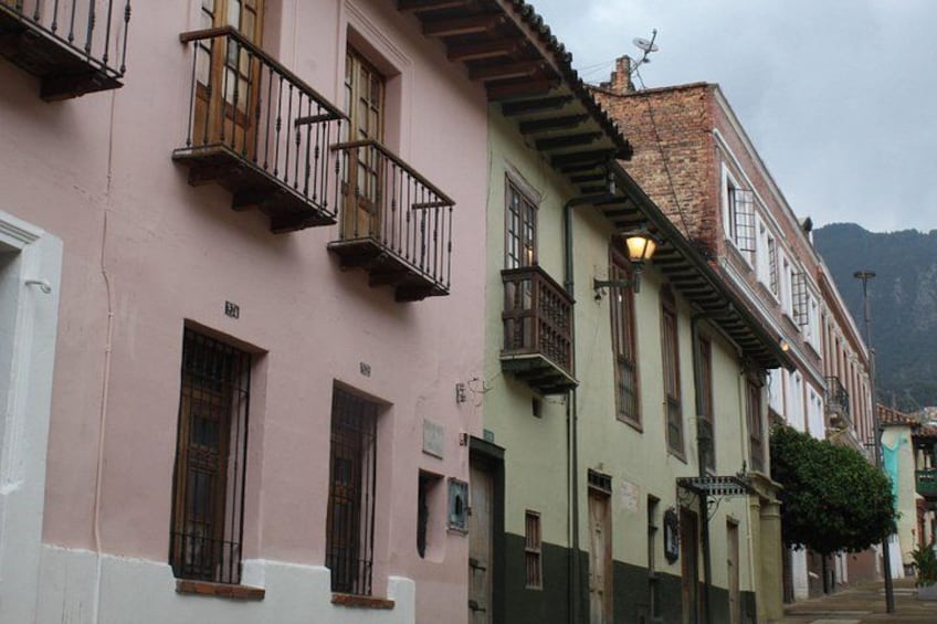 A street with pastel-colored buildings, balconies, and a mountain in the background. 2