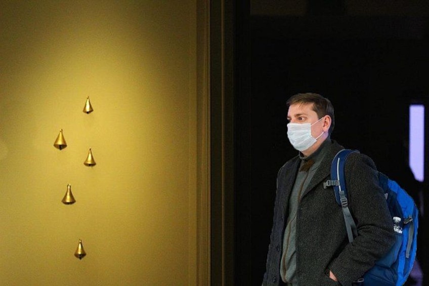 A person standing in a hallway with a blue backpack, a wall with golden light fixtures, and a door with a purple light. 4