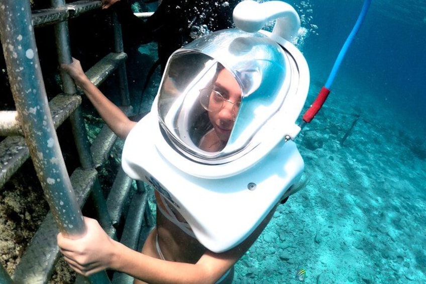 Una persona con casco de buceo descendiendo por una escalera al agua. 2