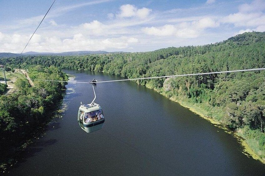 A cable car moving along a cable over a river surrounded by forested hills. 2