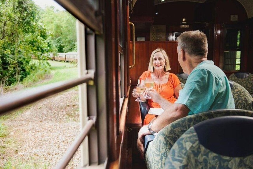 Two people sitting by a train window, a grassy landscape, and a wooden interior. 4