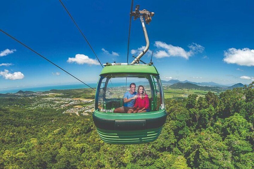 A cable car with two passengers, a green cable car, and a lush green landscape with mountains in the background. 1