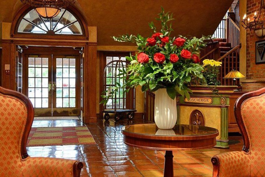 Un vestíbulo con un gran jarrón de rosas rojas, un piano y una escalera. 2