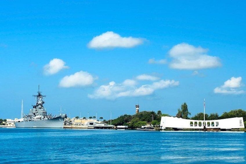 Un gran buque de guerra atracado en un muelle, una lancha blanca y un faro al fondo. 2
