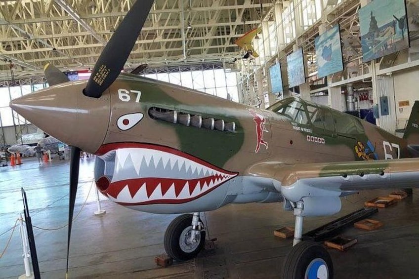 A military aircraft with a shark mouth painted on the nose, inside a hangar. 4