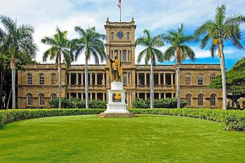 A large historic building with a clock tower, surrounded by a well-manicured lawn and palm trees. 2