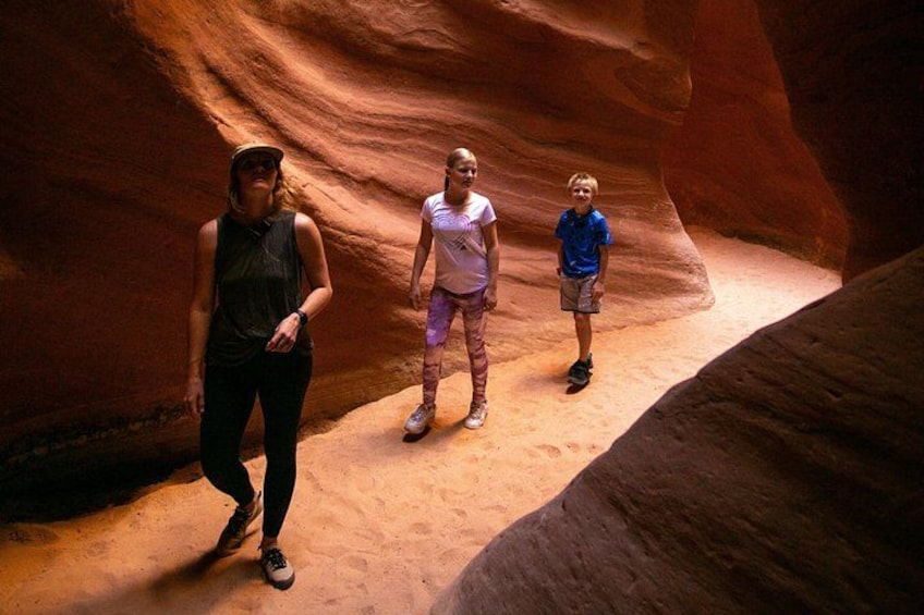 Three people standing in a narrow canyon with reddish-brown rock walls. 4