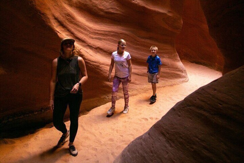 Three people standing in a narrow canyon with reddish-brown rock walls. 5