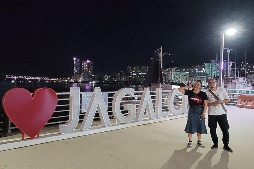 A couple posing in front of a large sign with the word 'JAGALDI' and a heart symbol. 5