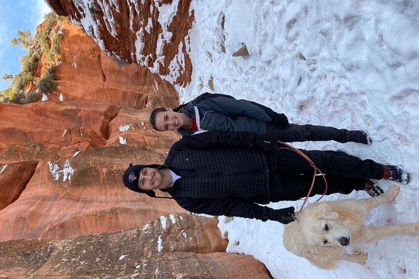 Two people standing in a snowy landscape with red rock formations. 2