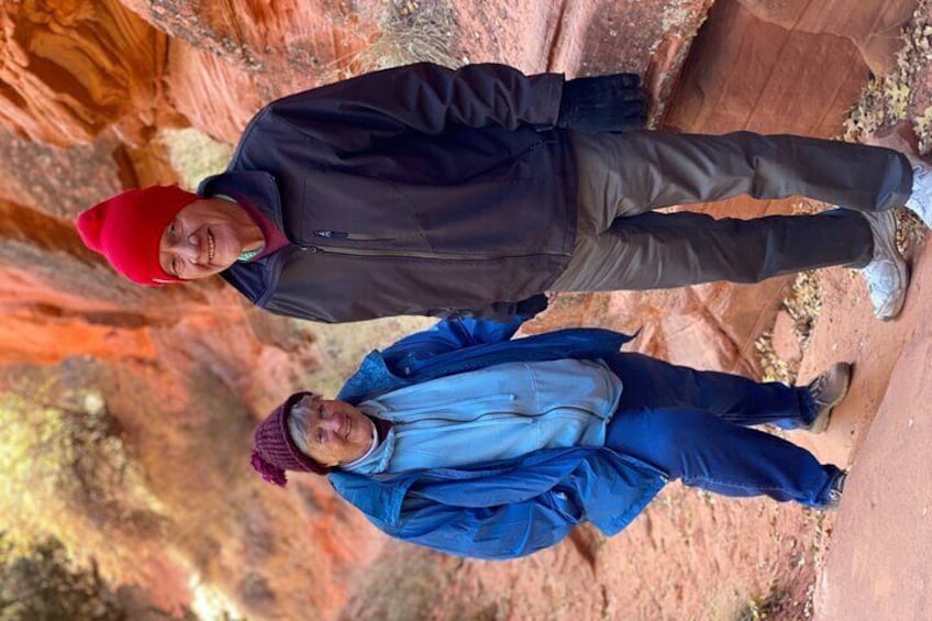 Two people standing on a rocky terrain with red rock formations in the background. 5