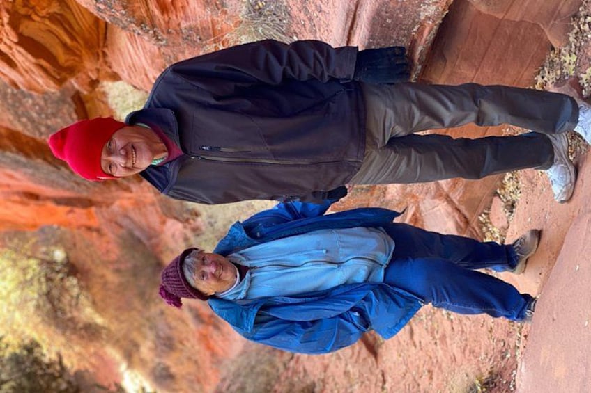 Two people standing on a rocky terrain with red rock formations in the background. 5