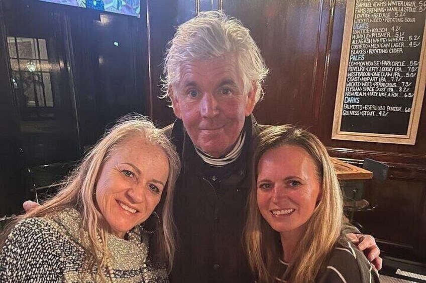Three people posing in a bar with a menu on the wall. 3