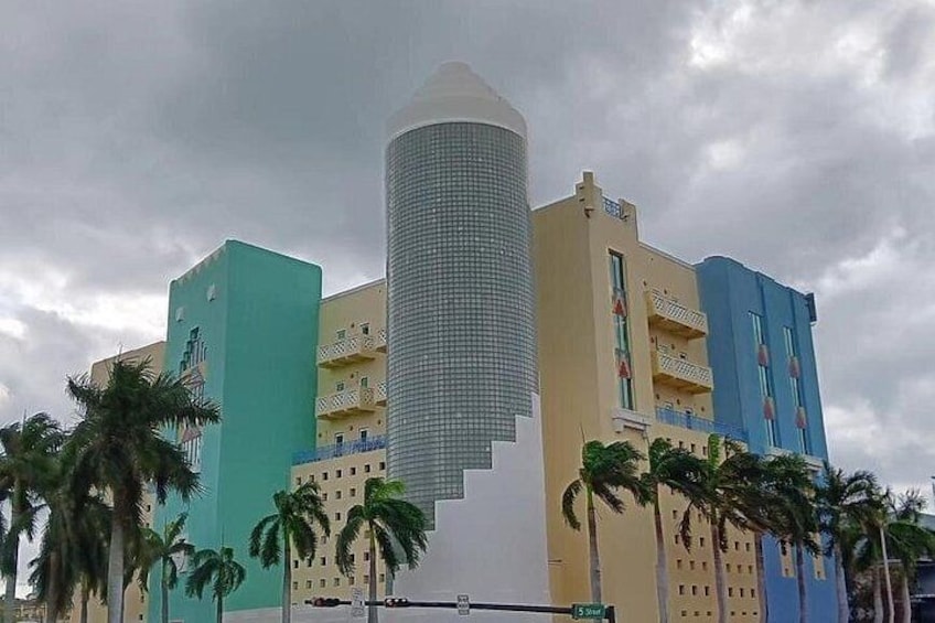 A multi-story building with a cylindrical tower, surrounded by palm trees and other colorful buildings. 4