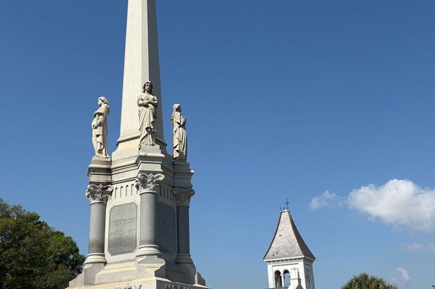 Ein hohes Denkmal mit Statuen und einem Kirchturm im Hintergrund. 1