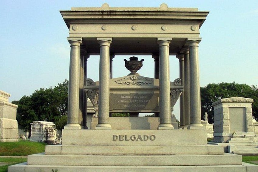 Ett nyklassicistiskt monument med kolonner och en central urna, där namnen ”Samuel DelGado” och ”Virginia” är inristade. 5