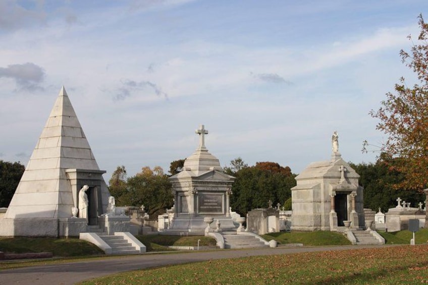 Ein Friedhof mit verschiedenen Denkmälern und Grabsteinen, darunter ein markantes, pyramidenförmiges Denkmal und mehrere Kuppelbauwerke. 3