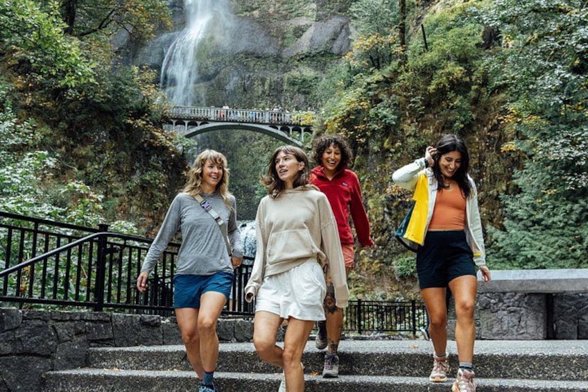 Un grupo de personas caminando sobre escalones de piedra en un área boscosa, con una cascada al fondo. 2