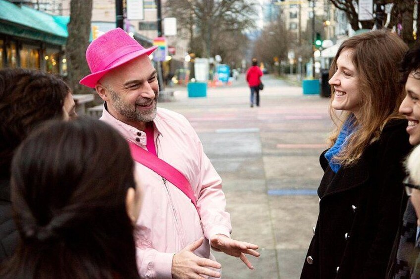 A person in a pink hat and jacket standing on a sidewalk, engaged in conversation with others. 5