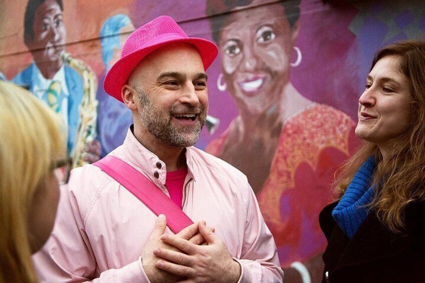 A person wearing a pink hat and a pink shirt standing in front of a mural. 1
