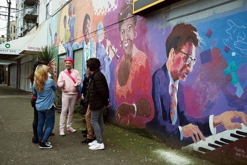 A mural with people standing in front of it, a building with a sign that reads 'WEST END', and a tree. 5