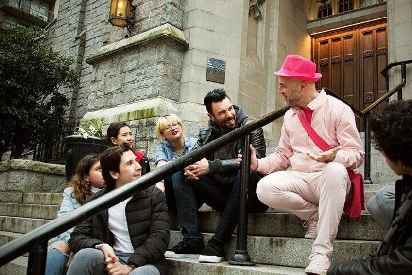 A group of people sitting on steps in front of a stone building with a wooden door and a metal railing. 2