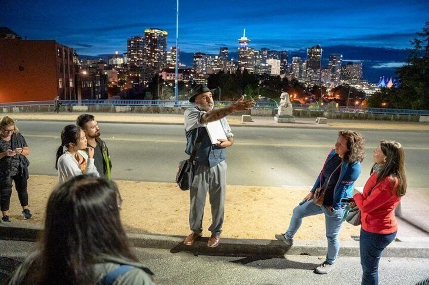 Un grupo de personas en una calle urbana de noche, con el perfil del horizonte de la ciudad al fondo. 5