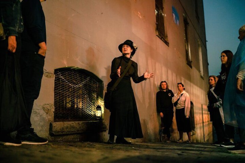 Une personne vêtue d’une longue robe noire et d’un chapeau fait des gestes devant un groupe de personnes qui se tiennent dans une rue, la nuit. 5