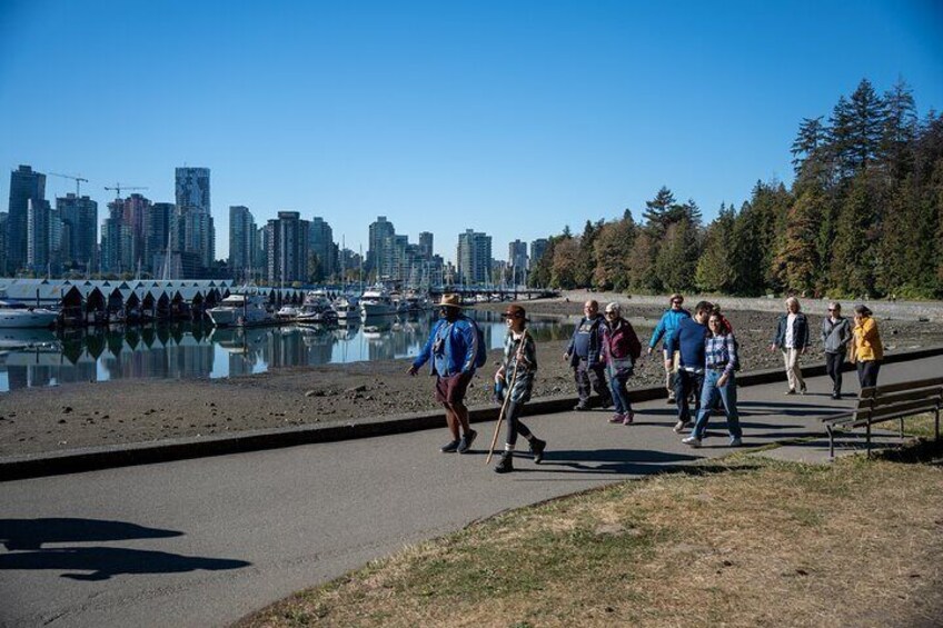 People walking along a waterfront path with a city skyline in the background. 3
