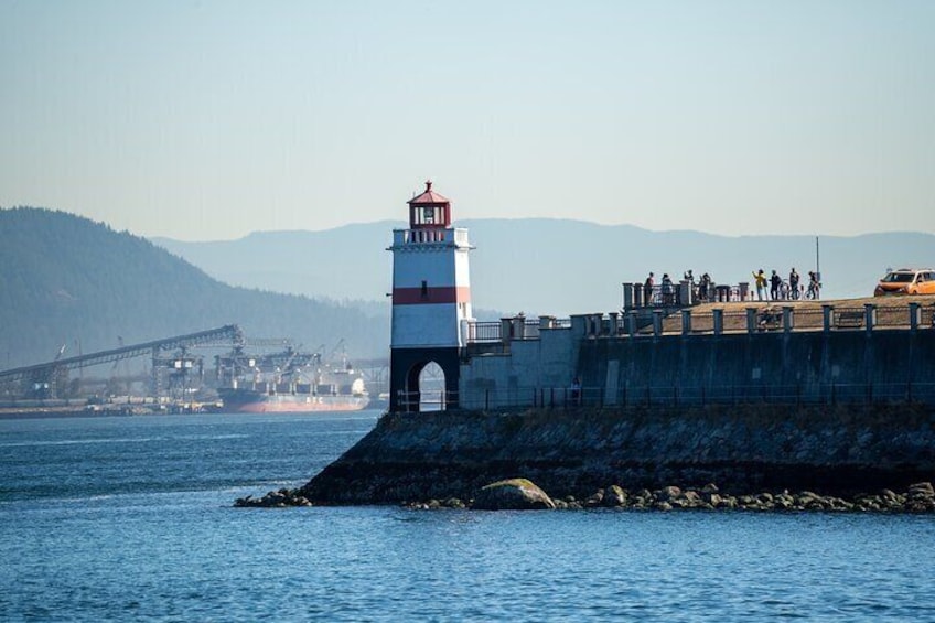 A lighthouse, a bridge, and a rocky shoreline with people on a viewing platform. 4