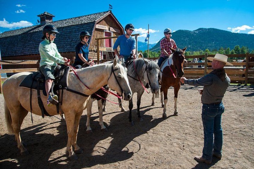 Un grupo de personas a caballo en un entorno al aire libre, con una construcción de madera y montañas al fondo. 2