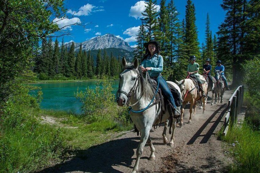 Un grupo de personas montando a caballo por un sendero, con un lago y montañas al fondo. 2
