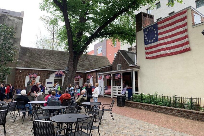 Ein Straßencafé mit Tischen und Stühlen, eine große amerikanische Flagge und ein Backsteinhaus im Hintergrund. 5