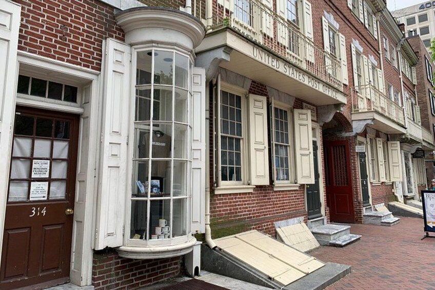 Ein historisches Backsteingebäude mit roter Tür, Erkerfenster und einem Schild mit der Aufschrift 'United States Post Office'. 4