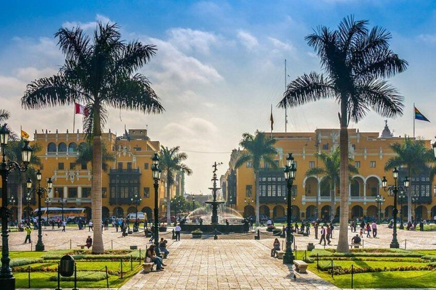 A plaza with palm trees, a fountain, and yellow buildings. 2