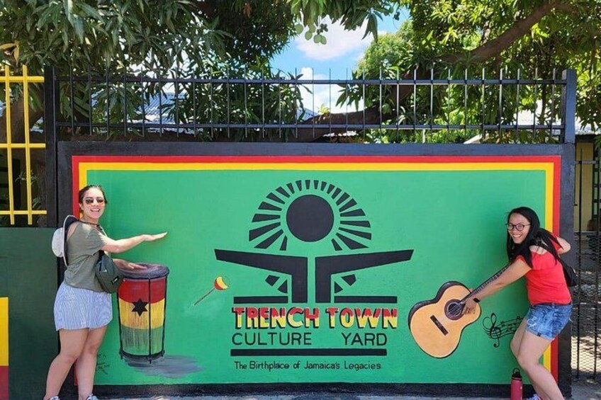 Et mural med en sol, en tromme og en guitar, med titlen 'Trench Town Culture Yard'. 3
