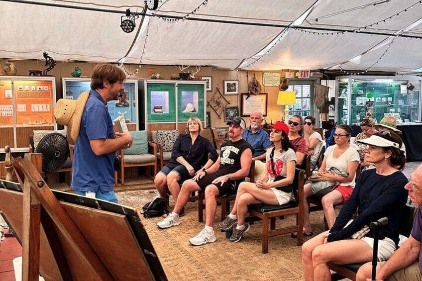 A group of people seated in a tented area with art supplies and framed pictures on the walls. 3