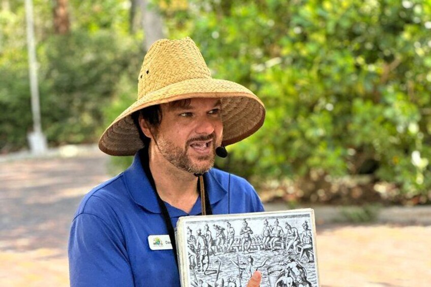 A person holding a book with illustrations, wearing a blue shirt and a straw hat. 1