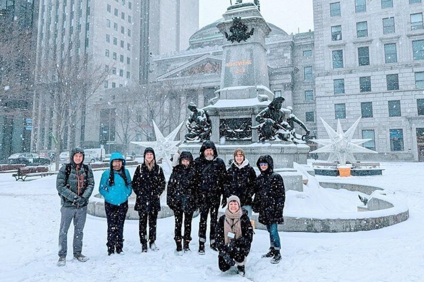 Un grupo de personas de pie en una plaza nevada con una fuente y estatuas al fondo. 2