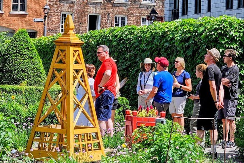 Eine Gruppe von Personen steht draußen in der Nähe eines gelben Gebäudes, mit einem Backsteinhaus und viel Grün im Hintergrund. 3