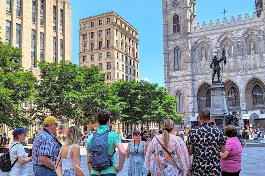 A group of people standing in a plaza with a historic building and a statue in the background. 3