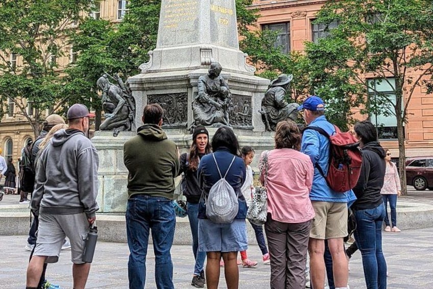En gruppe mennesker samlet omkring et historisk monument med inskriptioner og skulpturer. 2