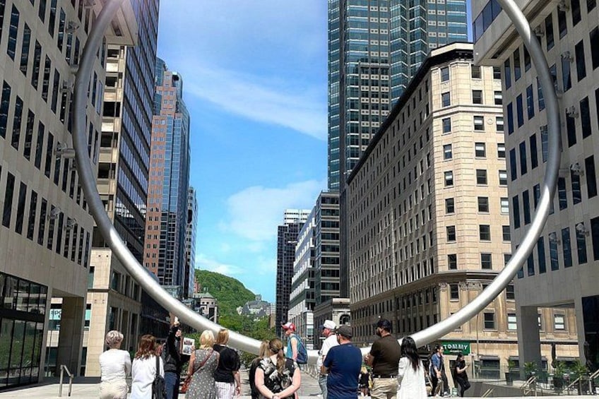 En stadsgata med höga byggnader, en böjd metallkonstruktion och människor som promenerar. 2