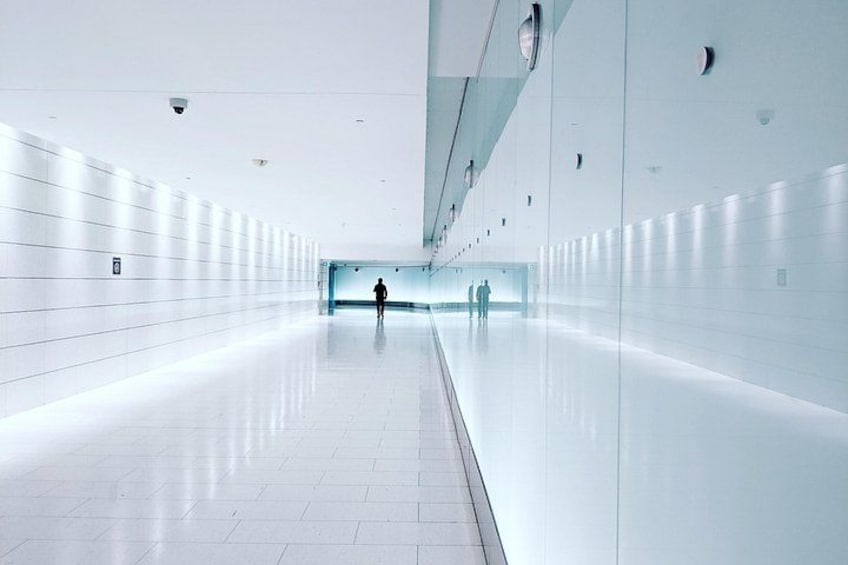 A long, white-tiled corridor with a reflective floor and walls, leading to a blue-lit tunnel. 4